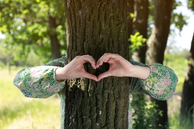 Woman hugging tree trunk and forming heart with hands in forest