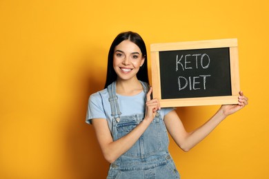 Photo of Happy woman holding chalkboard with words Keto Diet on yellow background