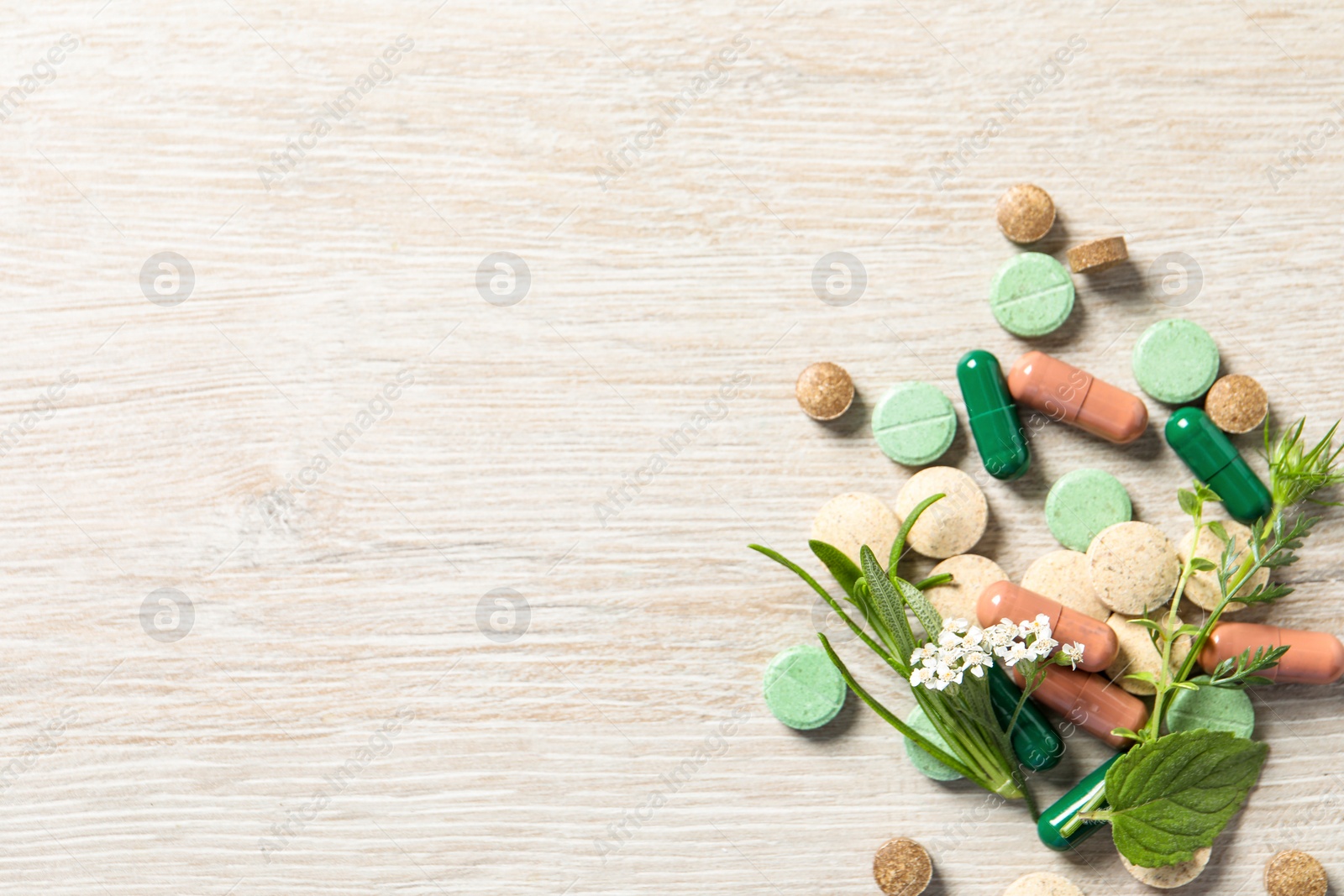 Photo of Different pills and herbs on wooden table, flat lay with space for text. Dietary supplements