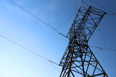 High voltage tower against beautiful blue sky, low angle view
