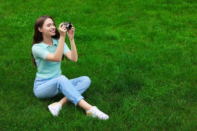Photo of Young woman with camera taking photo on green grass outdoors, space for text. Interesting hobby