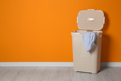 Photo of Open laundry basket with clothes near orange wall indoors, space for text