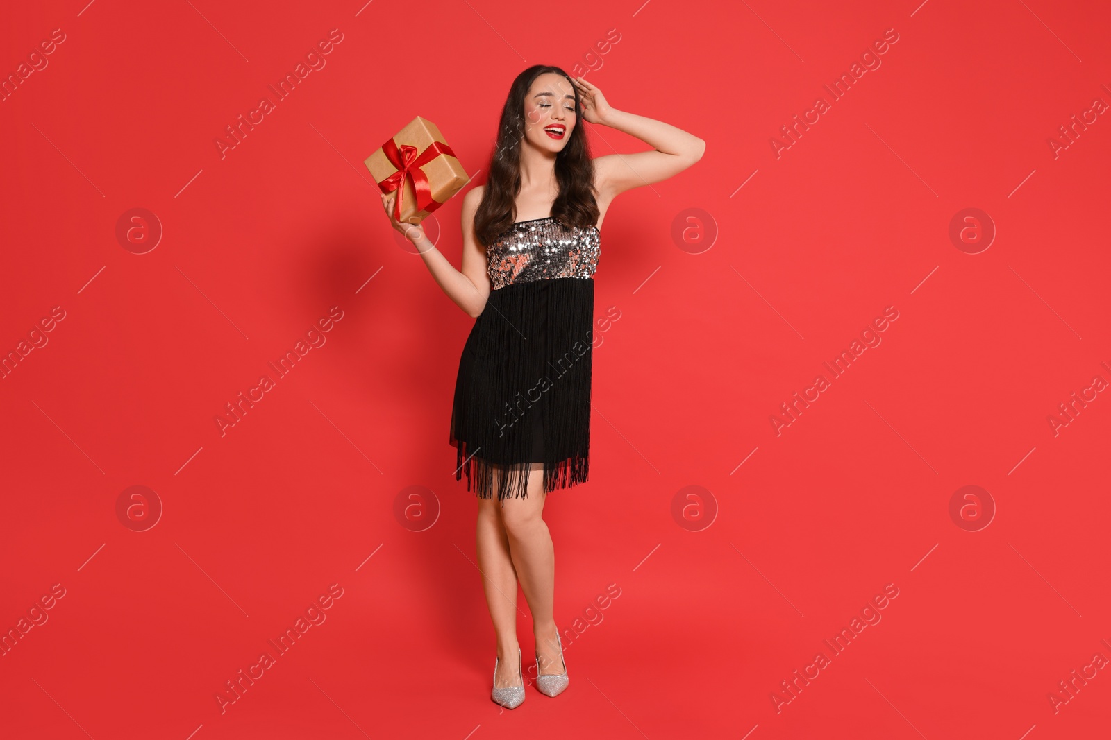 Photo of Beautiful young woman with Christmas gift on red background