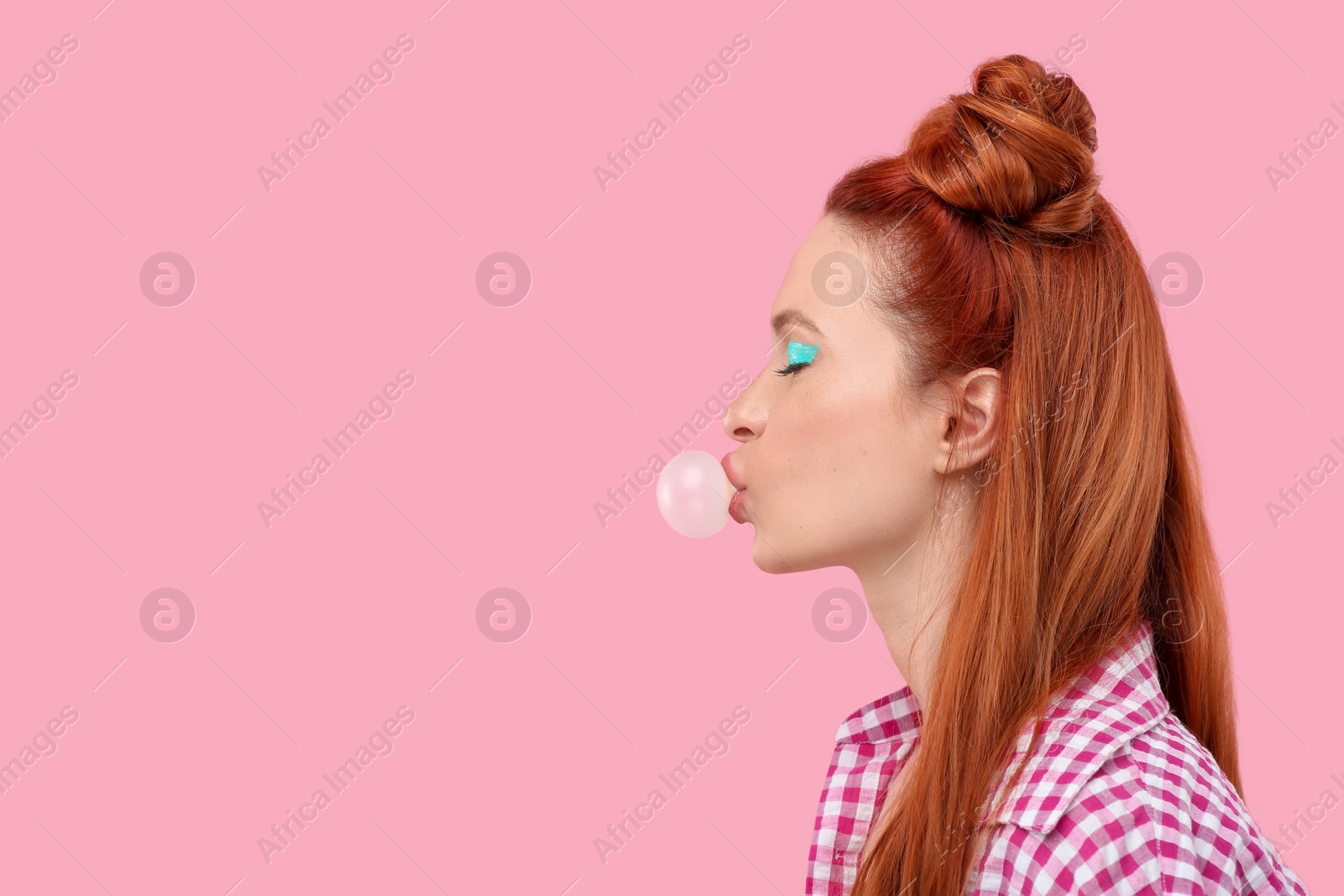 Photo of Beautiful woman with bright makeup blowing bubble gum on pink background. Space for text