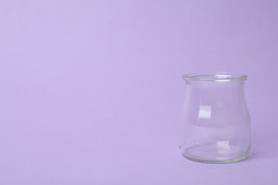 Open empty glass jar on lilac background, space for text