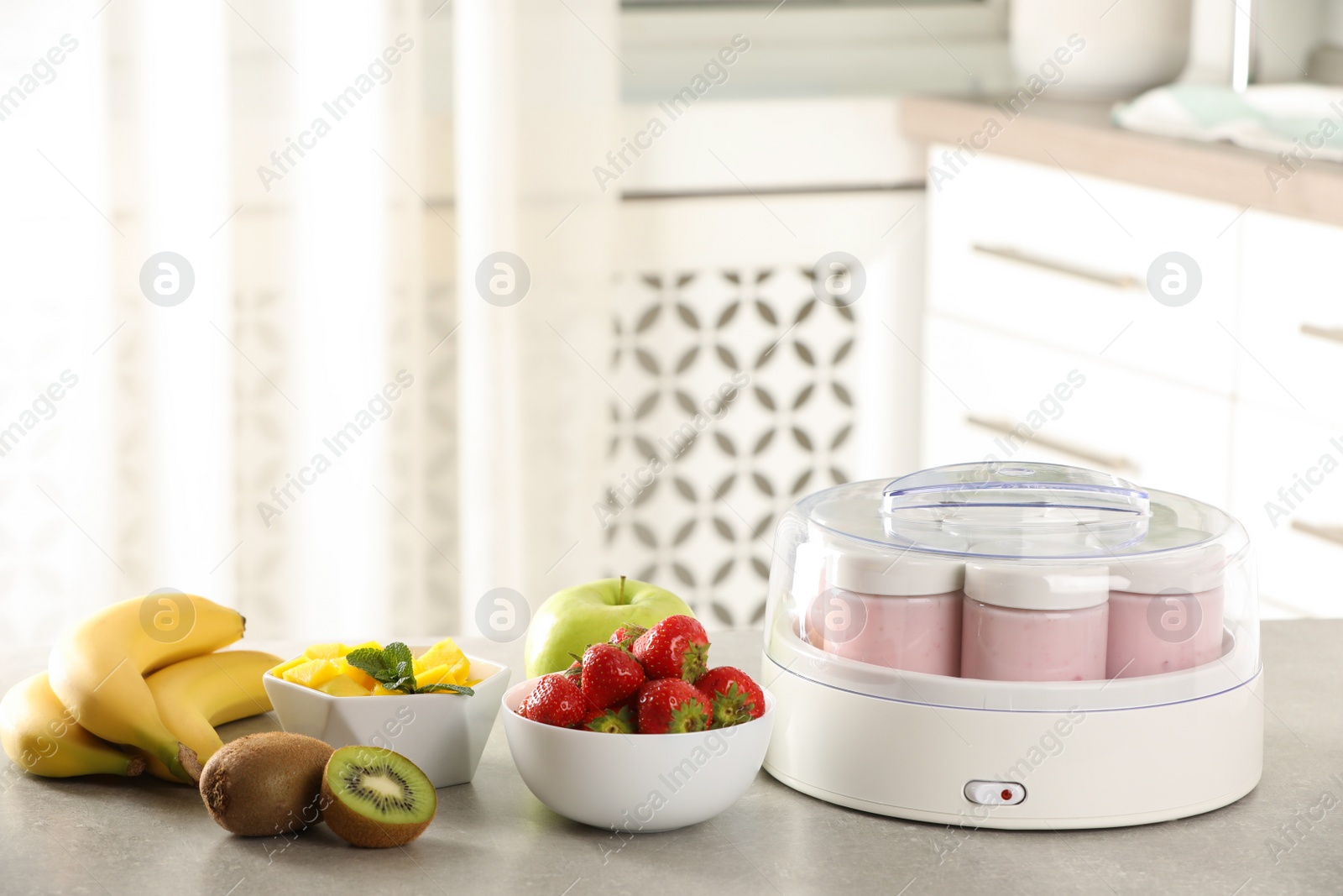 Photo of Yogurt maker with jars and different fruits on light grey table in kitchen