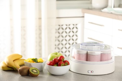 Yogurt maker with jars and different fruits on light grey table in kitchen