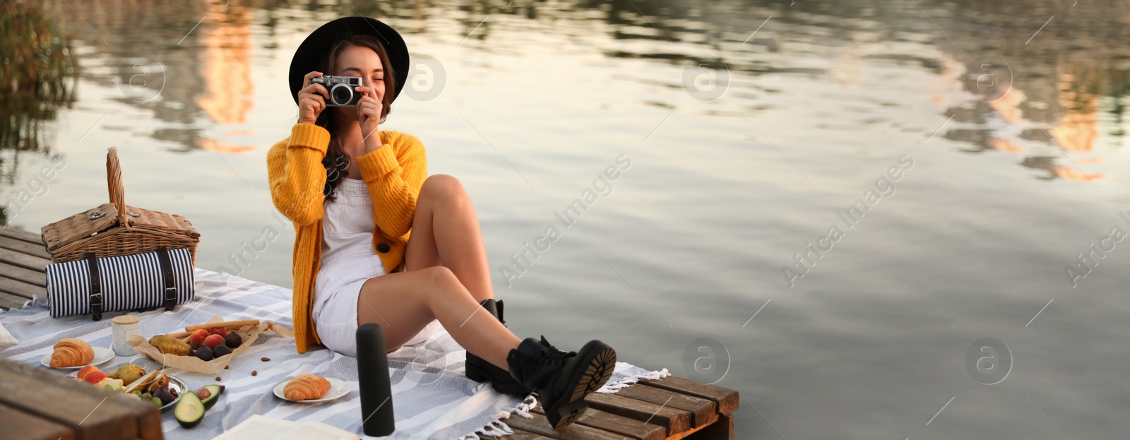 Image of Young woman taking picture with camera on pier at picnic. Banner design