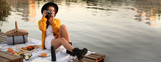 Image of Young woman taking picture with camera on pier at picnic. Banner design