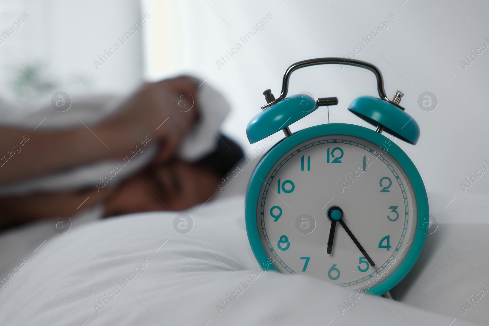 Photo of Sleepy man awaking at home in morning, focus on alarm clock. Space for text