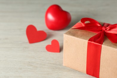 Photo of Beautiful gift box with decorative red hearts on white wooden table, closeup