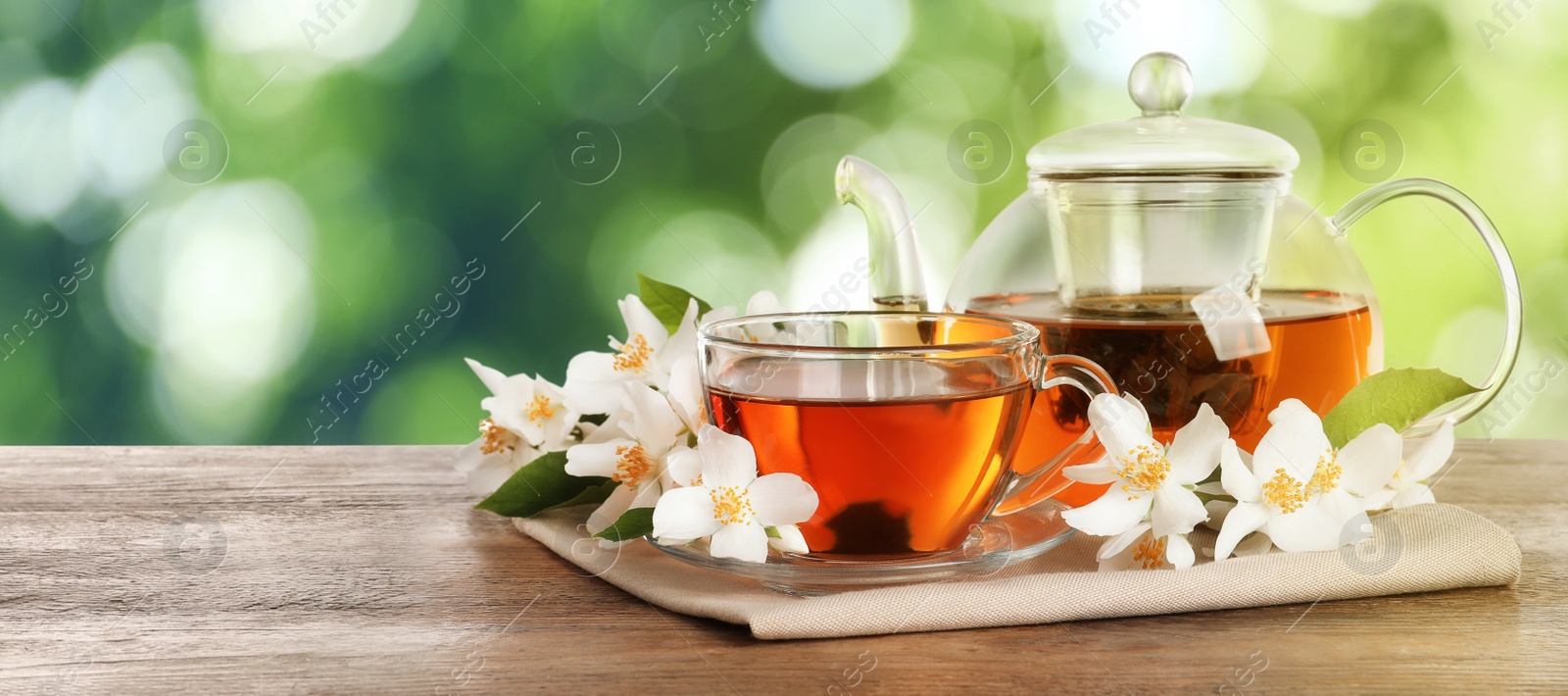 Image of Jasmine tea and fresh flowers on wooden table outdoors, space for text. Banner design