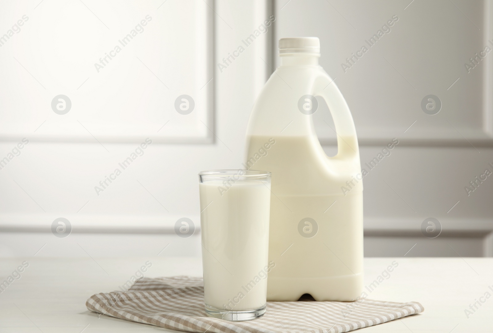 Photo of Gallon bottle and glass of milk on white wooden table