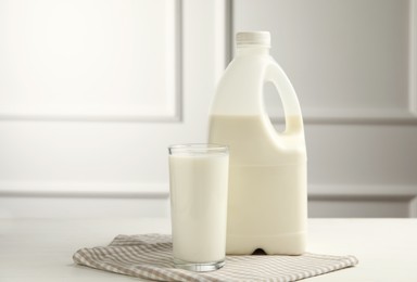 Gallon bottle and glass of milk on white wooden table