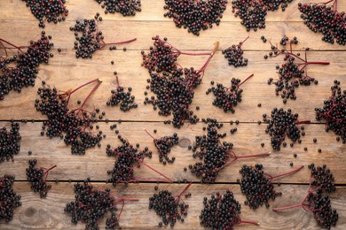 Photo of Many elderberries (Sambucus) on wooden background, flat lay