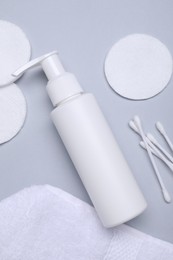 Bottle of face cleansing product, cotton pads and buds on light grey background, flat lay. Space for text