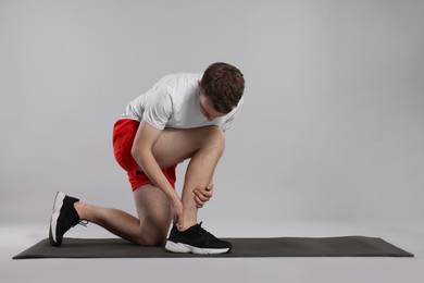 Photo of Man suffering from leg pain on mat against grey background. Space for text