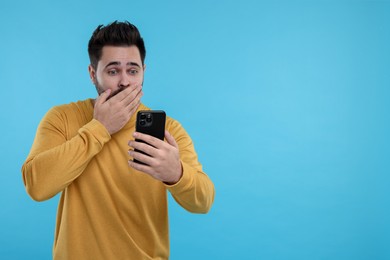Photo of Shocked young man using smartphone on light blue background, space for text