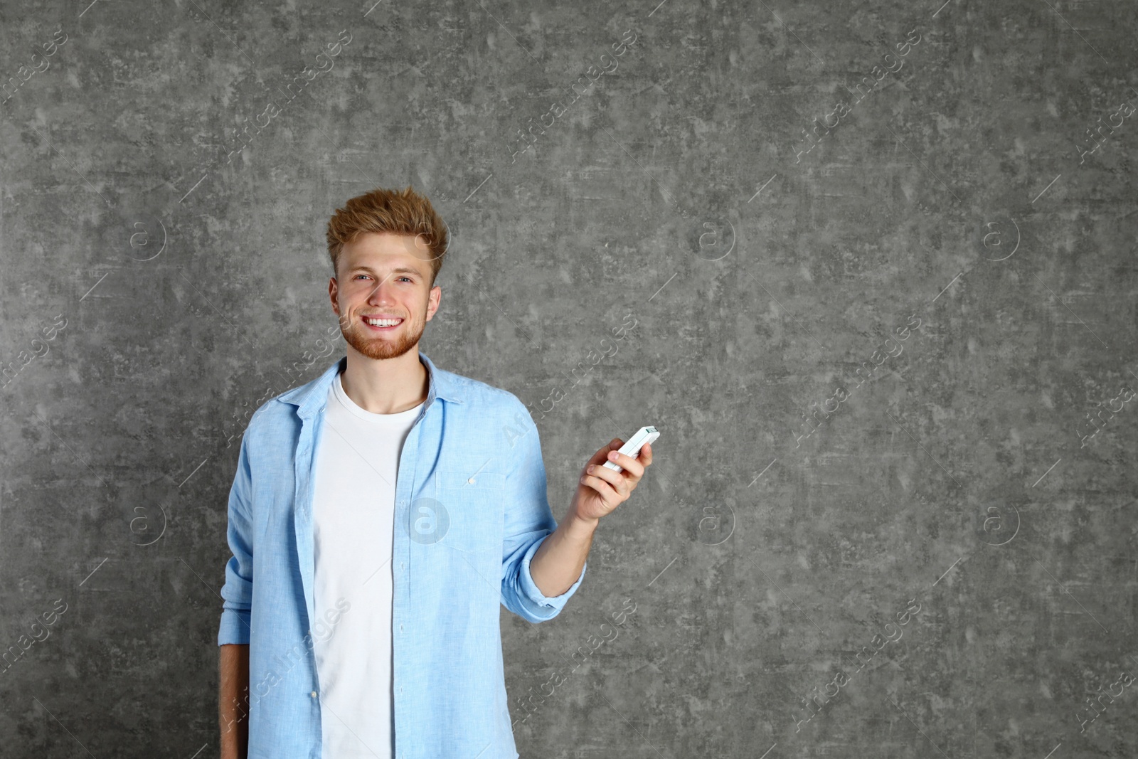 Photo of Young man with air conditioner remote on grey background. Space for text