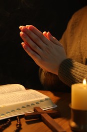 Photo of Woman praying at table with burning candle and Bible, closeup