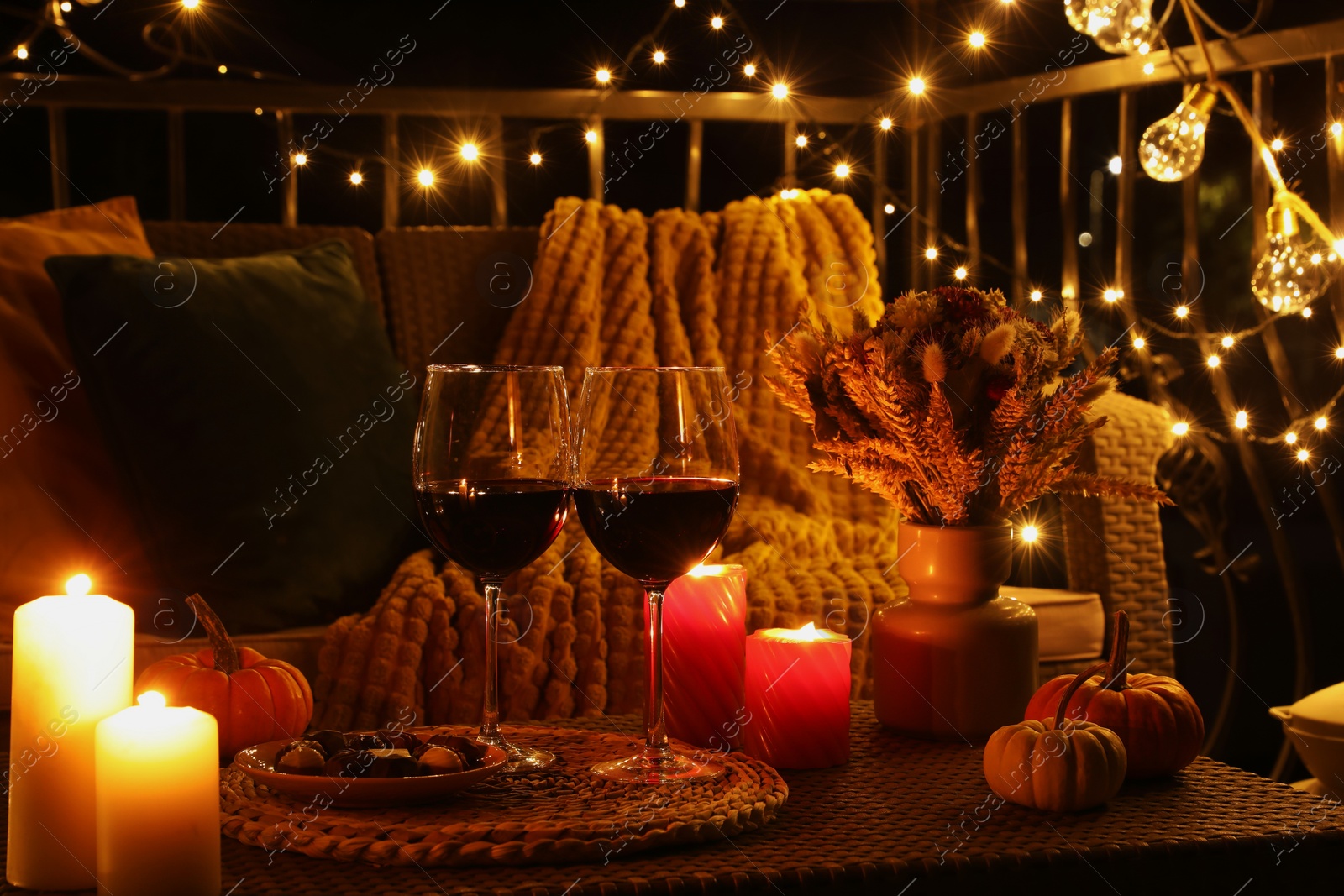 Photo of Glasses of wine, burning candles and autumn decor on outdoor terrace in evening