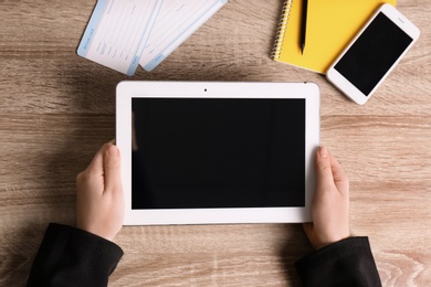 Woman holding tablet with blank screen on wooden background, top view. Travel agency