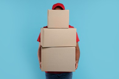Courier with stack of parcels on light blue background