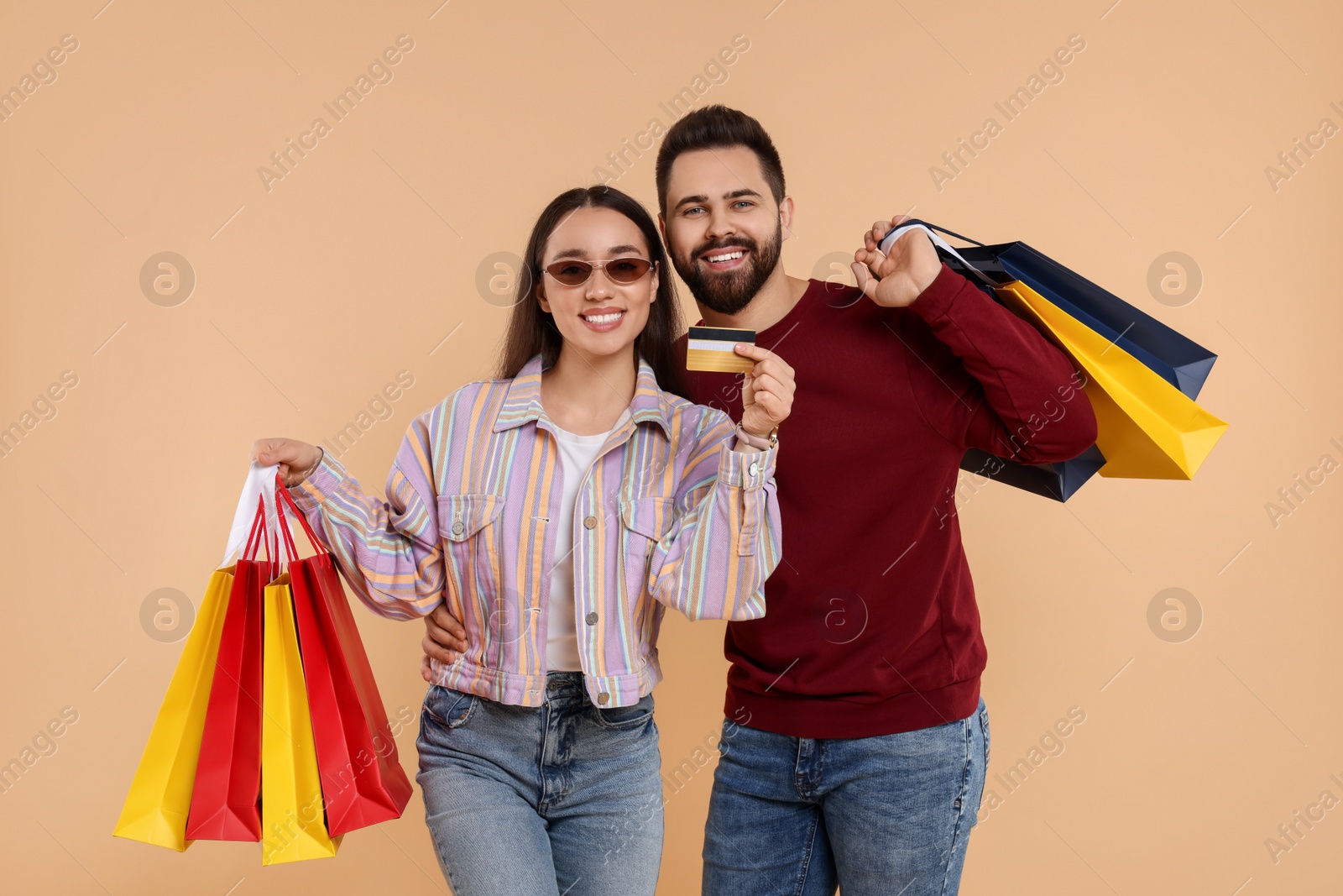 Photo of Happy couple with shopping bags showing credit card on beige background