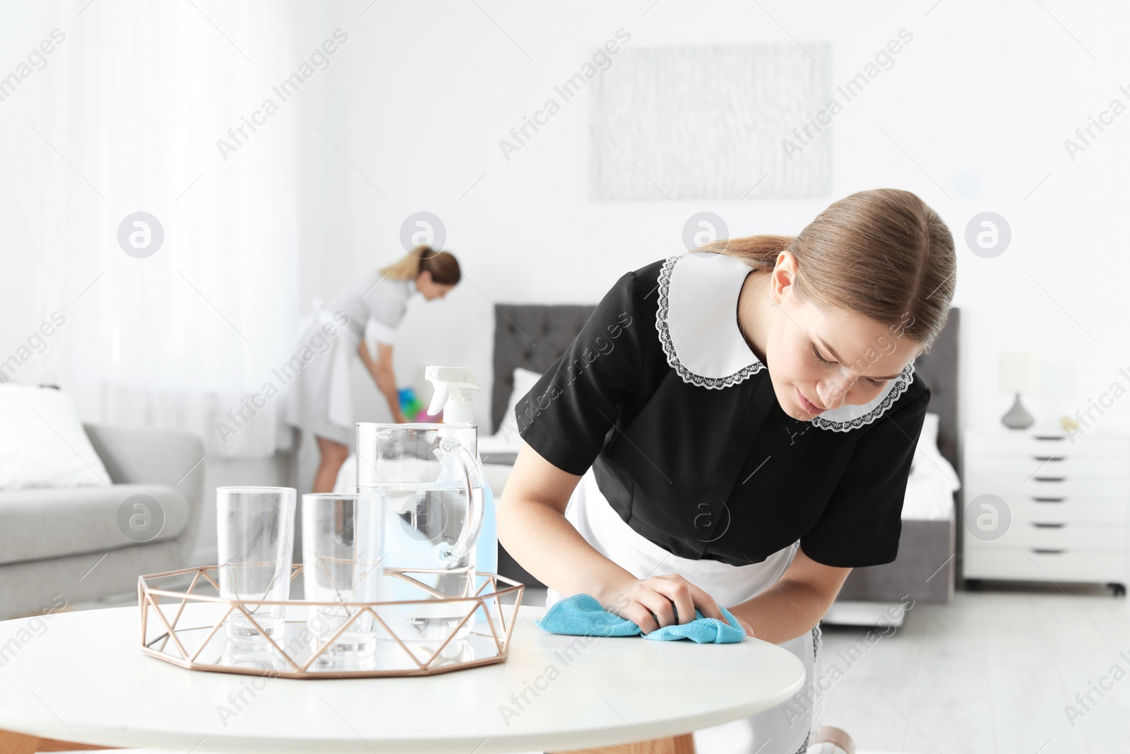 Photo of Young chambermaid cleaning table in hotel room