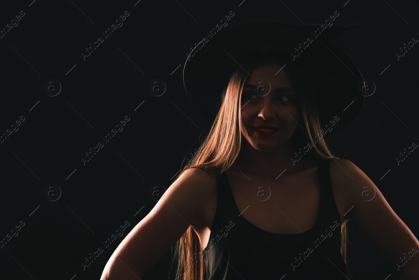 Photo of Young woman wearing witch costume on black background, space for text. Halloween party