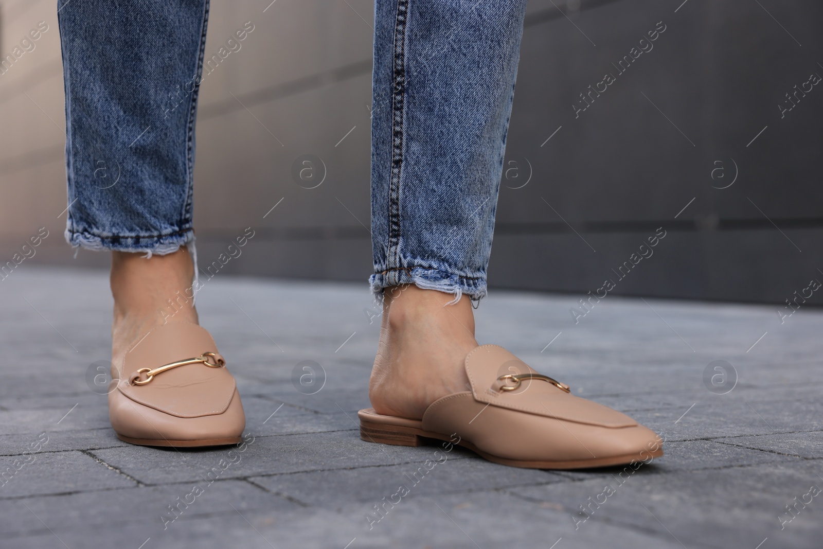 Photo of Woman in blue jeans and fashionable slippers walking on city street, closeup