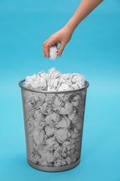 Woman throwing crumpled paper into metal bin on color background, closeup