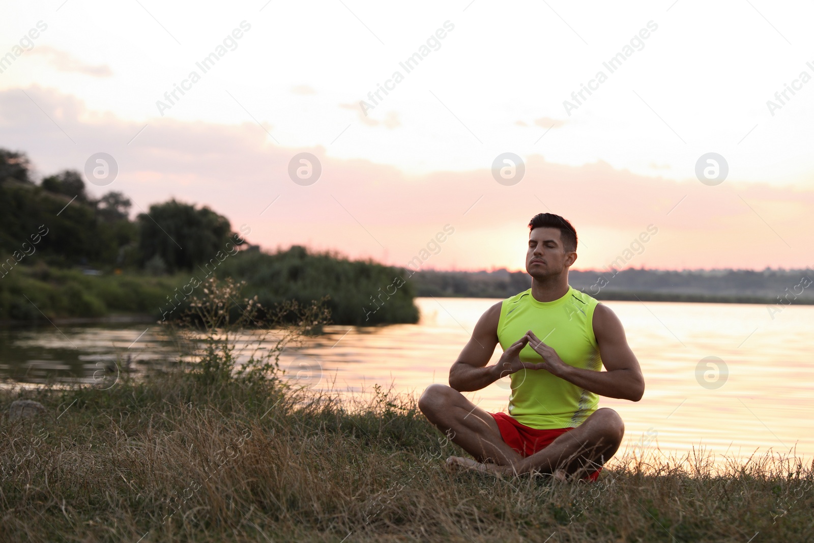 Photo of Man meditating near river in twilight. Space for text