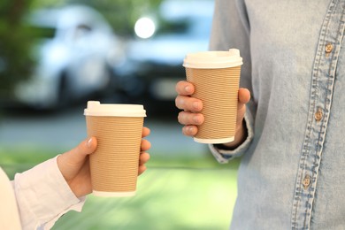 Women holding takeaway paper cups outdoors, closeup. Coffee to go