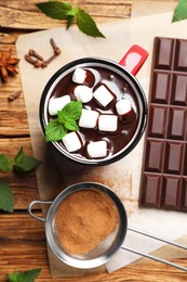 Photo of Mug of delicious hot chocolate with marshmallows and fresh mint near ingredients on wooden table, flat lay