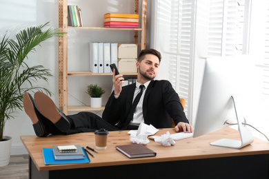 Photo of Lazy employee using smartphone while resting at table in office