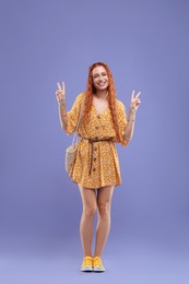 Photo of Stylish young hippie woman showing V-sign on violet background