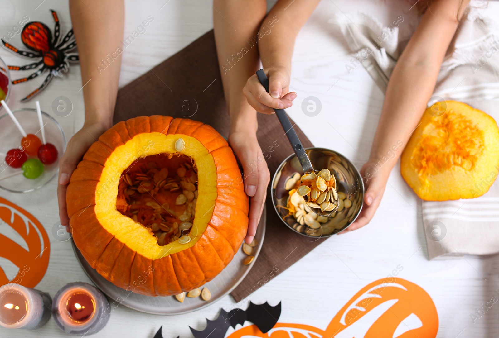 Photo of Mother and daughter making pumpkin jack o'lantern at white wooden table, top view. Halloween celebration