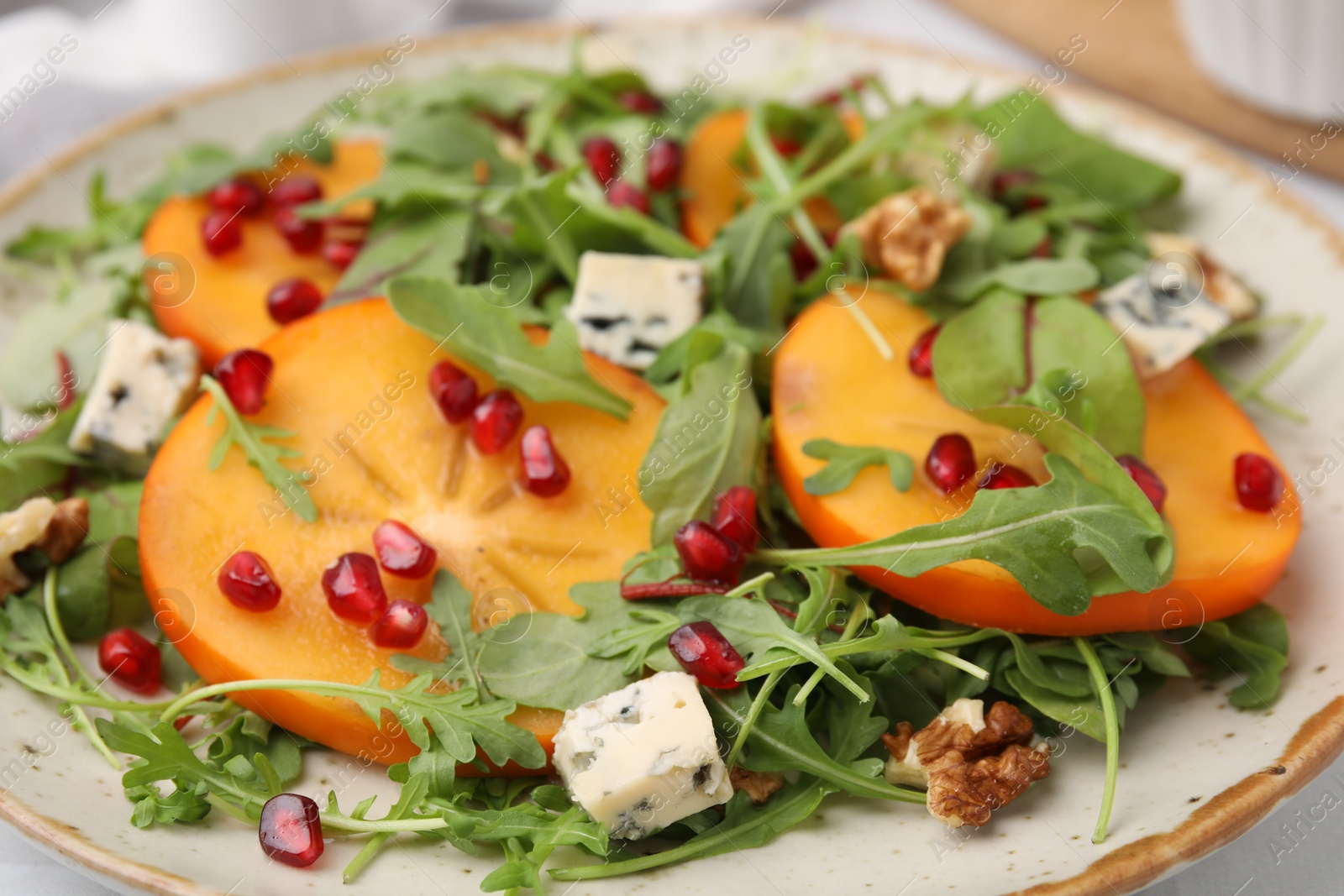 Photo of Tasty salad with persimmon, blue cheese, pomegranate and walnuts served on table, closeup