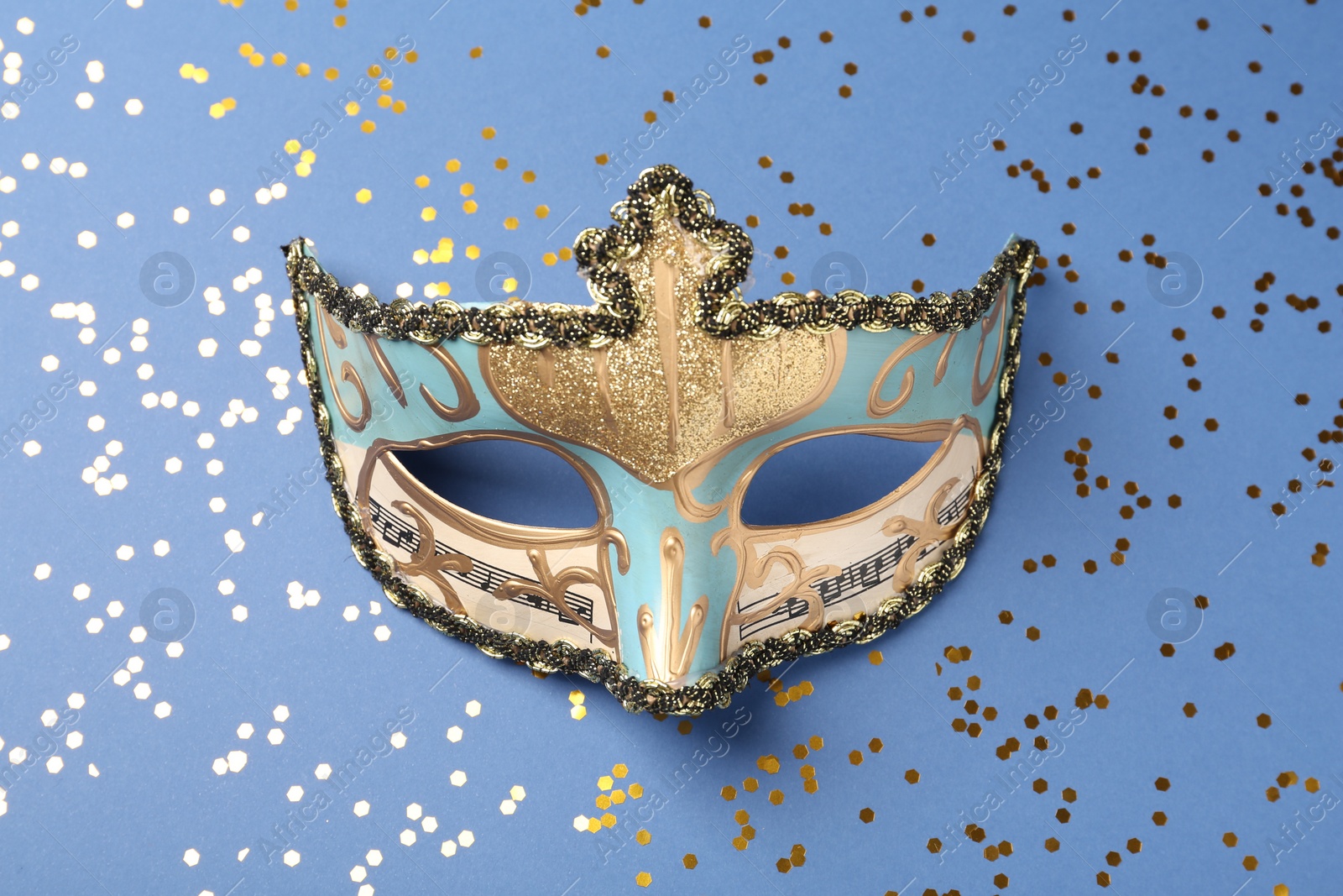 Photo of Beautiful carnival mask and shiny confetti on blue background, top view