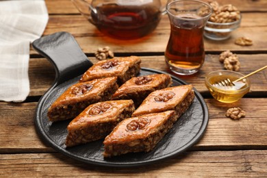 Photo of Delicious sweet baklava with walnuts, honey and hot tea on wooden table