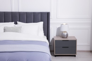 Comfortable bed near bedside table with lamp in stylish bedroom