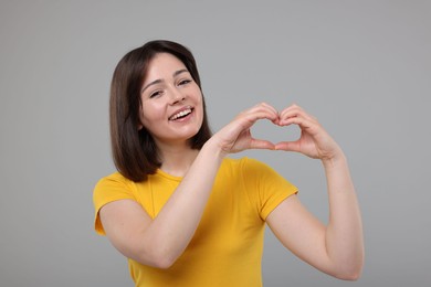 Photo of Happy woman showing heart gesture with hands on grey background