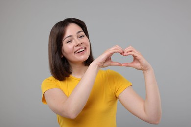 Happy woman showing heart gesture with hands on grey background