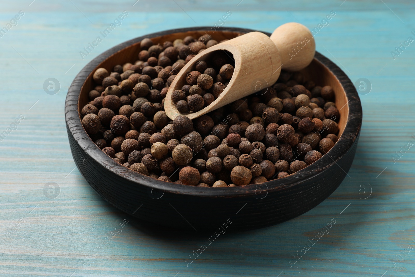 Photo of Aromatic allspice pepper grains in bowl and scoop on light blue wooden table