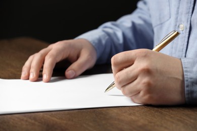 Photo of Man writing on sheet of paper with pen at wooden table, closeup