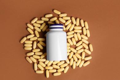 Plastic medicine bottle surrounded by pills on brown background, flat lay