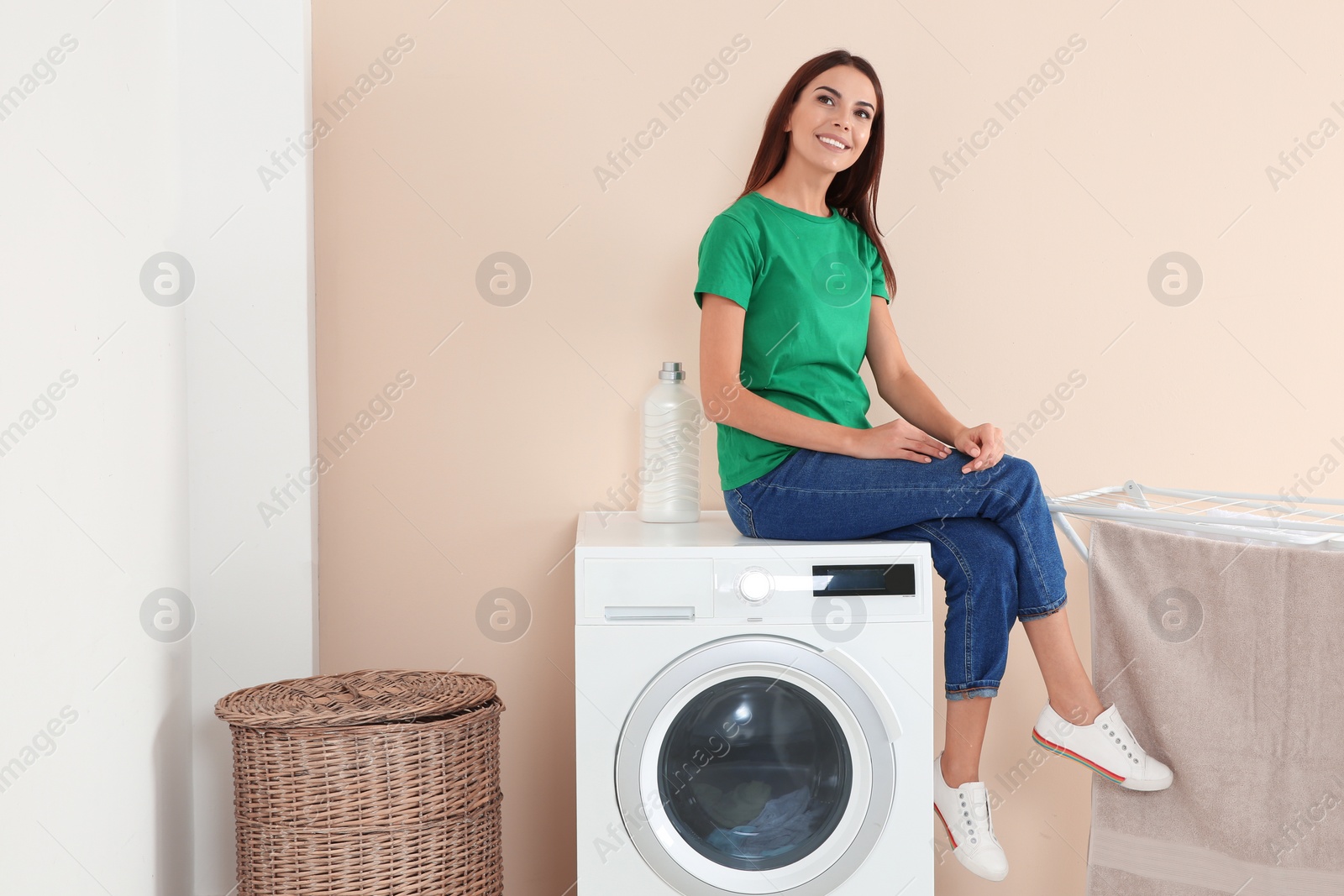 Photo of Young woman sitting on washing machine at home, space for text. Laundry day