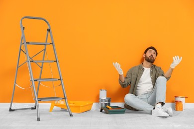 Photo of Emotional designer sitting on floor near freshly painted orange wall