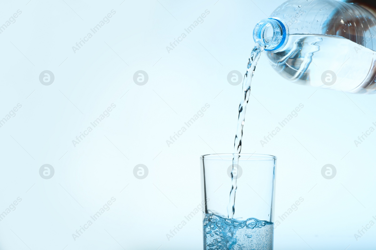 Photo of Pouring water from bottle into glass against blue background. Refreshing drink